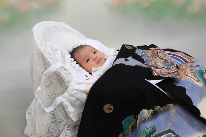 お宮参りの記念撮影 黒地の掛け着と白いおくるみの赤ちゃん